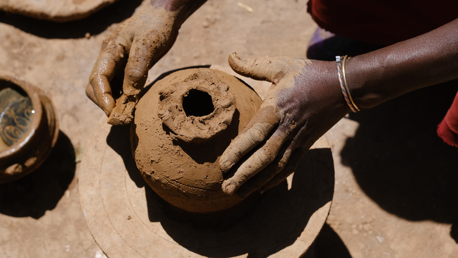 Clay-covered hands holding freshly shaped raw jebena coffee pot showing traditional Ethiopian pottery craftsmanship before firing